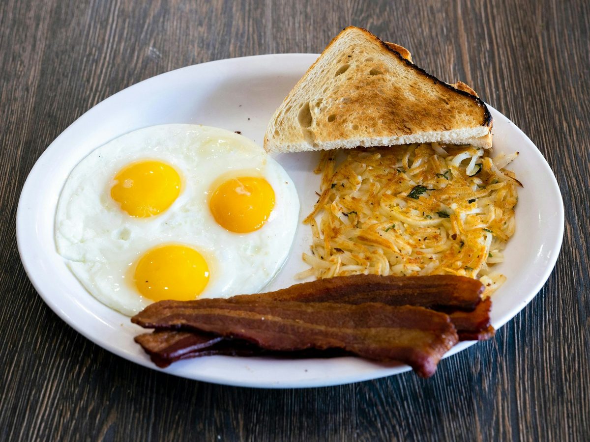 Two sunny-side-up eggs, hash browns, bacon and toast on a white plate — illustrative
