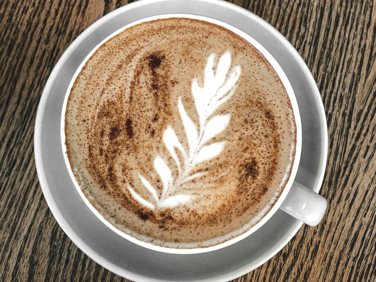 Latte with rosetta latte art in a white cup on dark wood — illustrative