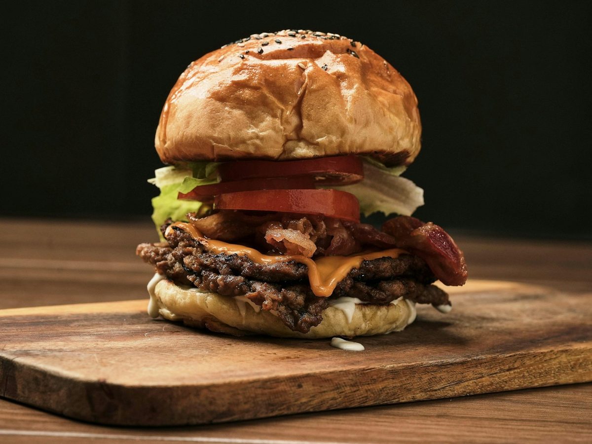 Bacon cheeseburger with lettuce and tomato on a wooden board — illustrative